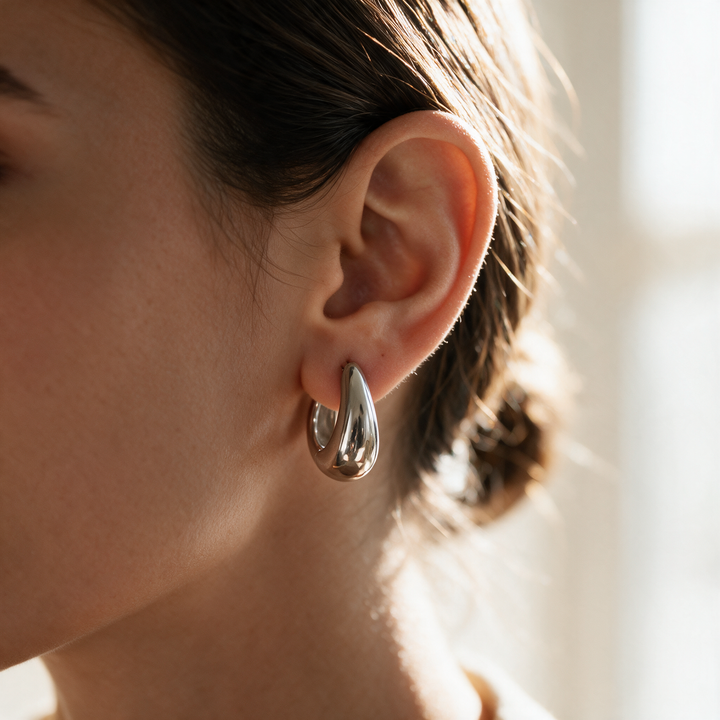 Chunky silver huggie hoop worn in ear, warm backlight