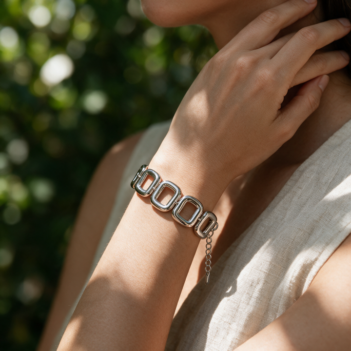 Silver bracelet worn on wrist, hand at neck, dappled greenery light