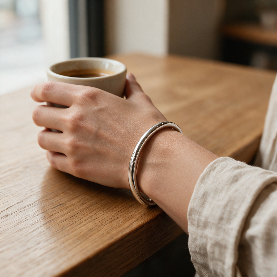 Silver bracelet worn on wrist holding espresso cup, café light