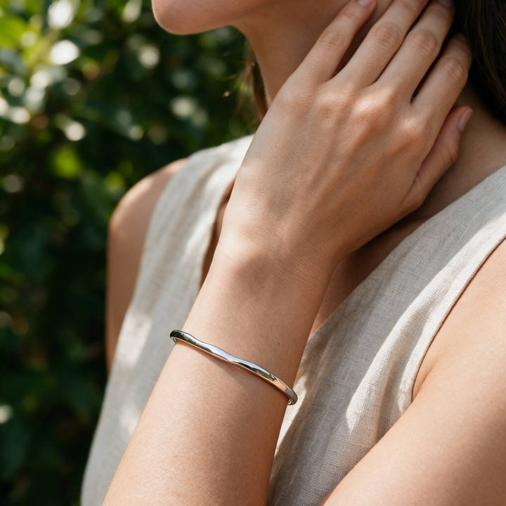 Silver bracelet worn on wrist, hand at neck, dappled greenery light
