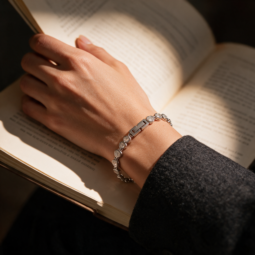Silver bracelet on wrist across open book, warm lamplight