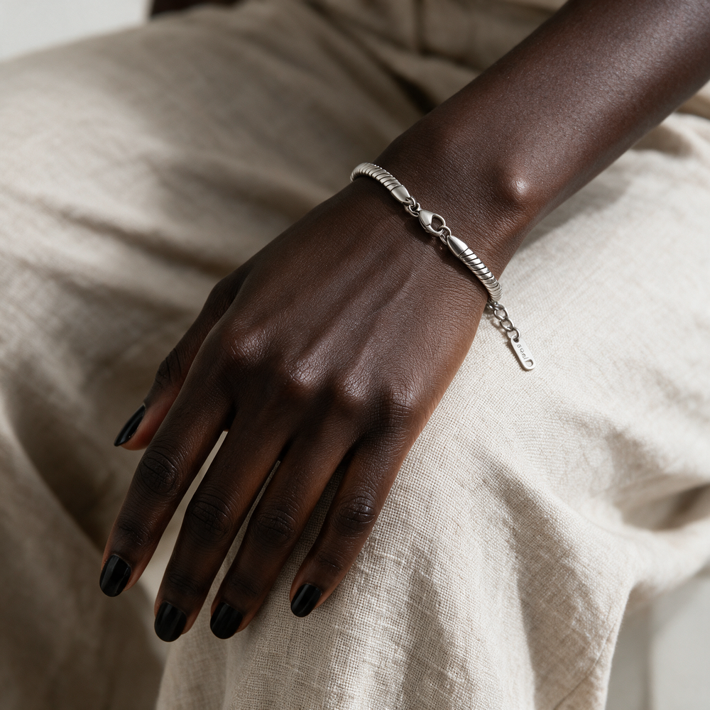 Silver bracelet on hand resting on linen trousers at knee