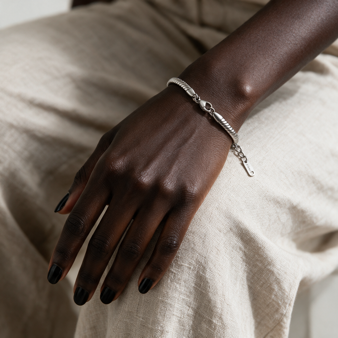 Silver bracelet on hand resting on linen trousers at knee