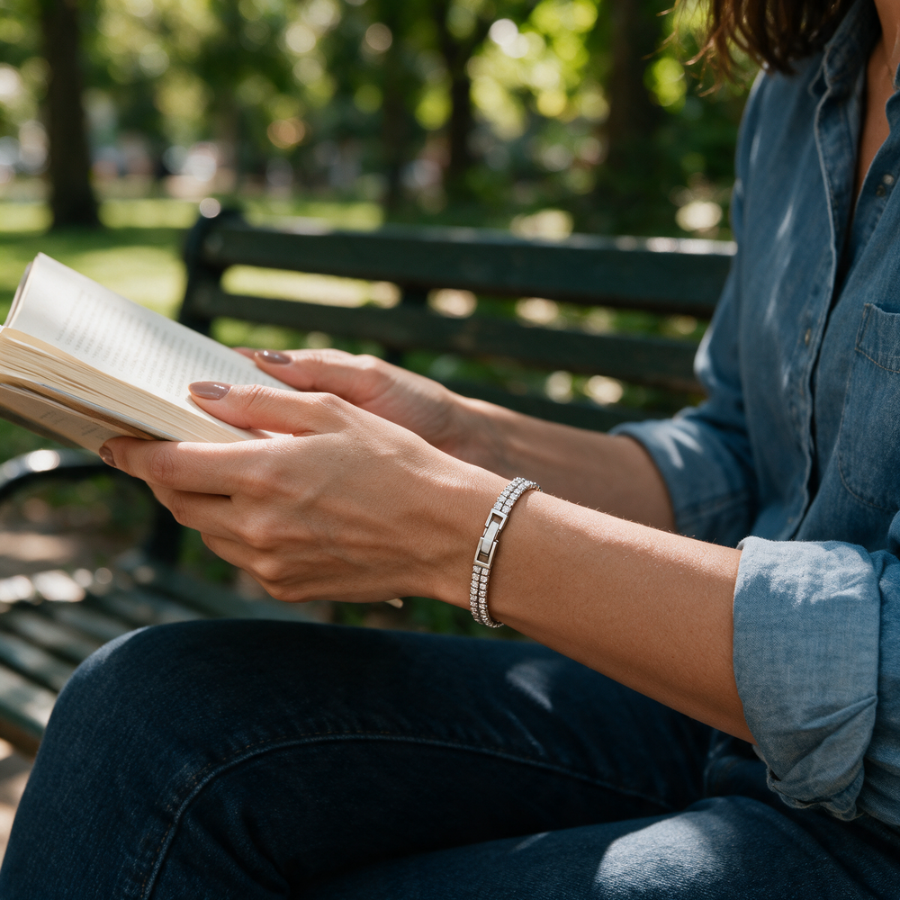 Silver bracelet on hands holding book on park bench