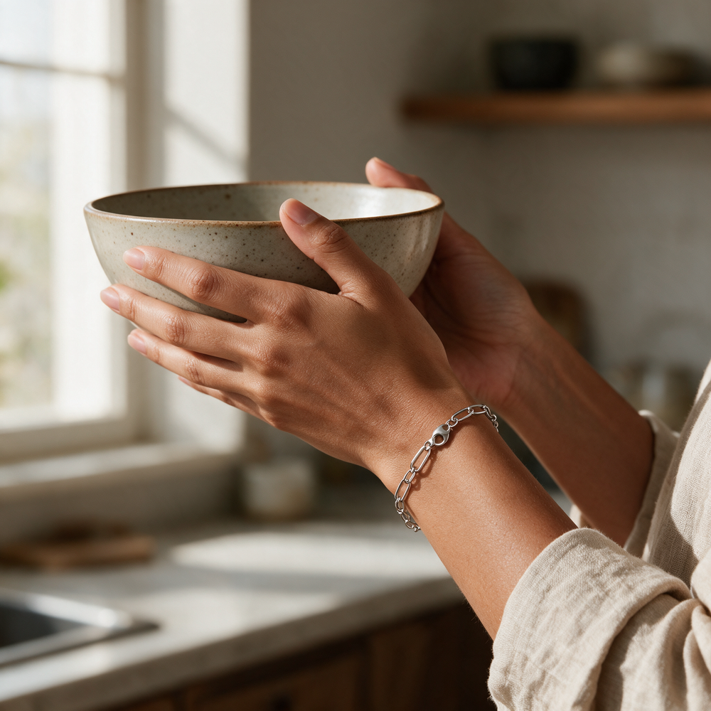 Silver bracelet on hands cradling stoneware bowl