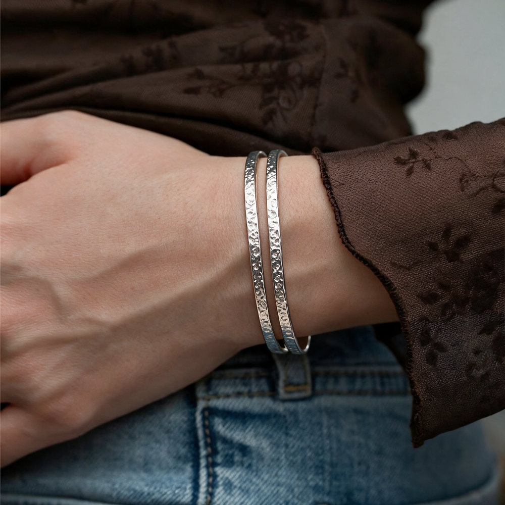 Silver bracelet worn on wrist, sheer brown blouse and denim